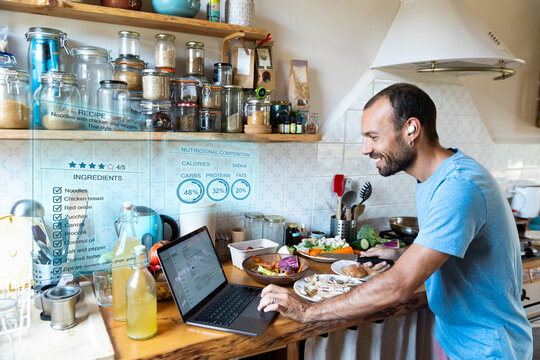 Man cooks healthy meal using laptop and hologram recipe