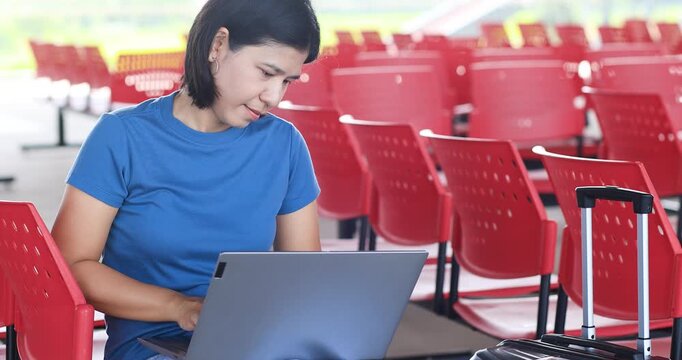 Young woman working on a laptop with luggage at Train station, Bus station, Airport waiting area, remote work, digital nomad lifestyle, business travel, productivity, and modern travel
