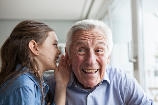 Granddaughter wispering something in the ear of her grandfather