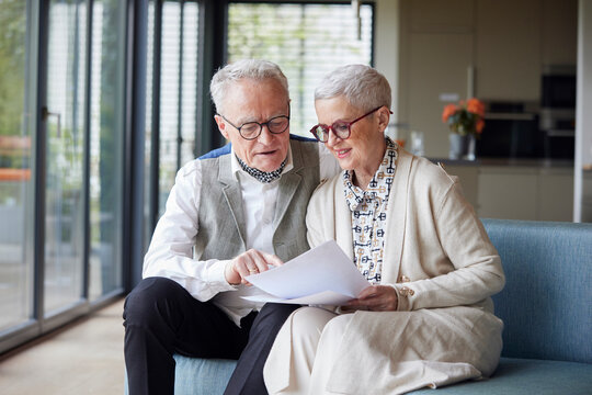 Senior couple sitting on couch at home reading document