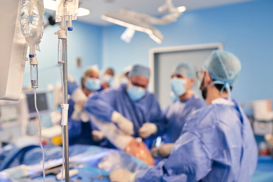 IV drip in operation room with doctors operating surgery in background