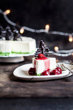 Piece of no-bake cheesecake, decorated with chocolate Christmas trees on plate with hot cherry sauce