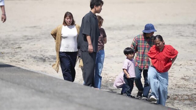 Family strolls beachside, enjoying sunny day. Children laugh, adults smile, all moving together. Perfect scene for family vacations, travel, or leisure content. No animals or plants visible