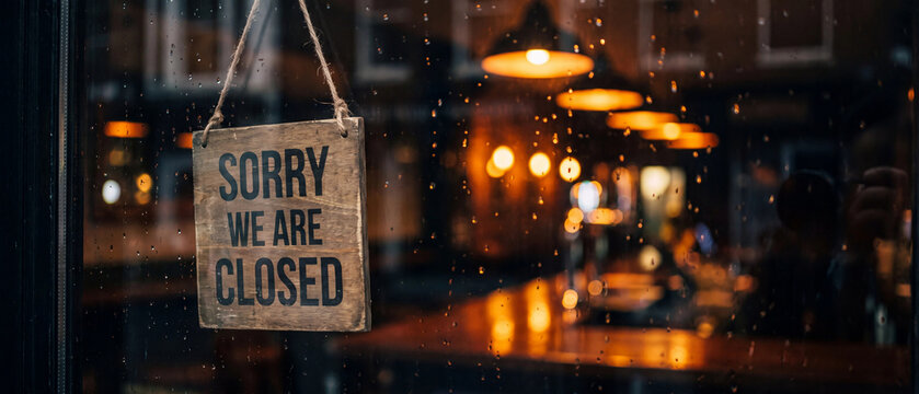 Closed sign hanging on a glass door of a pub or restaurant at night with rain droplets on the window and warm bokeh lights