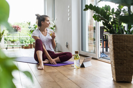 Woman drinks water while resting on a yoga mat at home