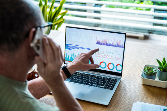 Man talking on smartphone and pointing at data on laptop screen