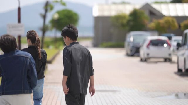 Three people walk together on a quiet street. Sunlight glows softly over the scene. They seem relaxed, enjoying the calm day. Perfect for tranquil urban or seaside scenes