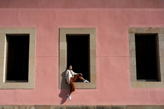 Asian woman sitting on window sill of building