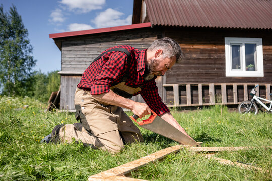 Carpenter working with hand saw cutting plank for playhouse on sunny day