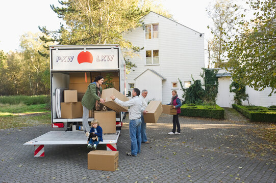 Family loads cardboard box into moving van outdoors