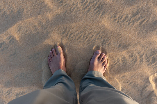 A high-angle first person POV shot of a traveler standing barefoot on the soft, golden sand dunes at the Inland Sea, Khor Al Adaid, Qatar during a desert safari.
