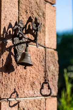 Vintage cast iron doorbell with chain mounted on brick wall, closeup. Antique bronze-colored metal door bell with pulling chain, attached to textured red brick corner wall under sunny outdoor light