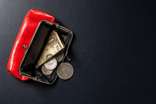 Open red leather purse with US dollar bill and coins. Top view of open small red leather coin purse containing one dollar banknote and silver American cents on textured black surface, copy space