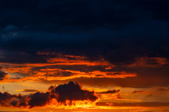 Dramatic sunset sky with dark storm clouds and fiery orange light. Beautiful evening sky filled with dark contrast clouds lit from below by brilliant fiery orange and yellow sunset