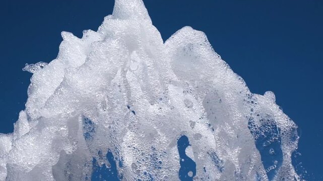Close-up of white fountain water jets against clear blue sky. Foamy splashes create refreshing abstract texture symbolizing freshness, summer, purity and movement