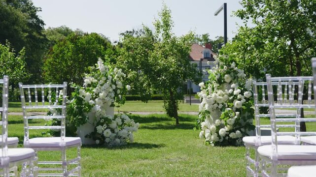 Wedding ceremony setup features elegant floral arrangements and clear chairs in a lush garden, creating a beautiful atmosphere for the event