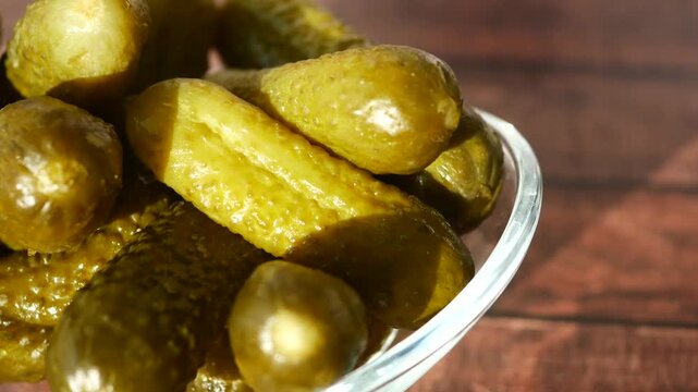 Macro rotating view of crunchy pickled cucumbers in glass bowl on wooden background with cinematic sunlight
