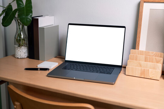 Laptop with blank white mockup screen on wooden desk in minimalist office.