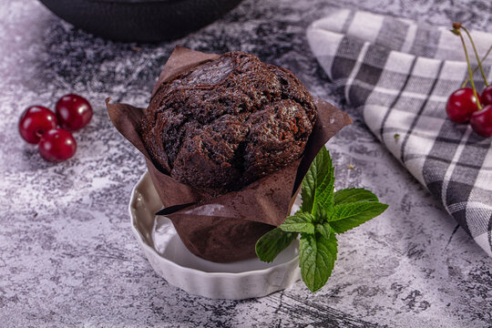 Chocolate muffin with fresh mint and cherries on rustic surface