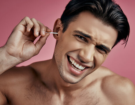 Young Man Uses Cotton Swab to Clean His Ear Against a Solid Pink Backdrop
