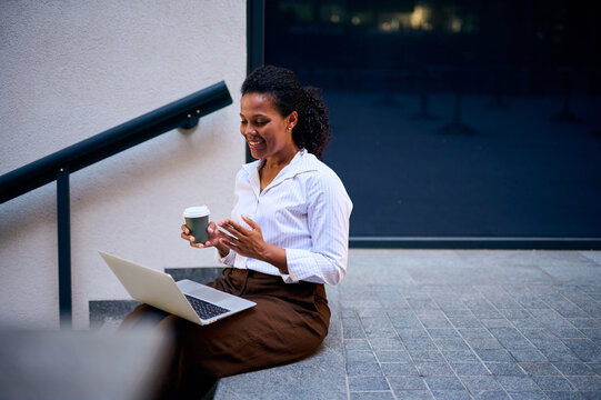 Smiling African American Woman Working Remotely With Laptop and Coffee on Urban Steps for Business