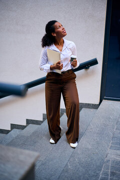 Confident African American Business Woman Walking Up Stairs With Laptop and Coffee for Workday