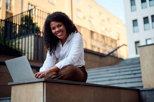 African American Woman Working on Laptop Outdoors on Urban Steps, Smiling Professional Remote Worker