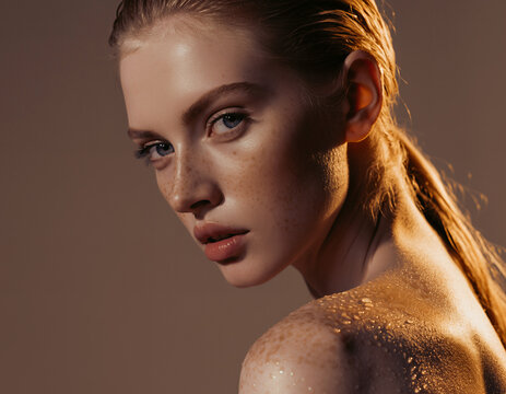 Close-up beauty portrait of a freckled woman with wet skin and golden light