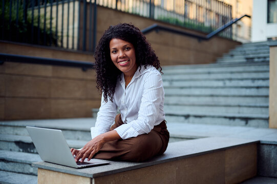 Smiling African American Woman Working Remotely With Laptop On Urban Steps For Business Branding