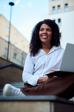 Confident African American Woman Working Remotely on Laptop Outdoors in Urban Business Setting