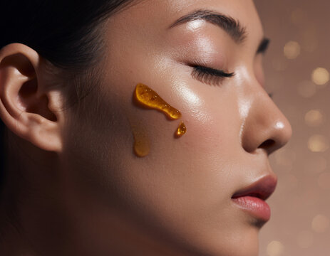 Golden Serum Droplets on Glowing Skin of a Woman with Eyes Closed Close-up