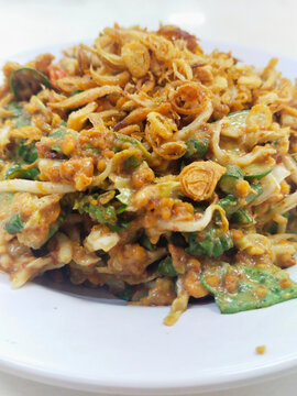 A plate of Karedok.  It is a raw vegetable salad from West Java, Indonesia includes long beans, cucumbers, bean sprouts, cabbage, lemon basil, small green eggplant, covered in peanut sauce dressing