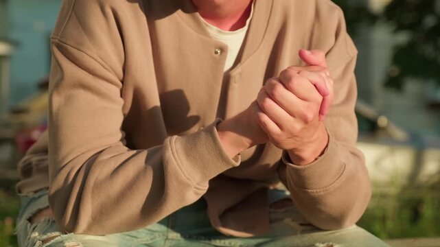Man doing a nervous hand gesture. Close up of a man sitting outdoors with his fingers and hands clasped together.