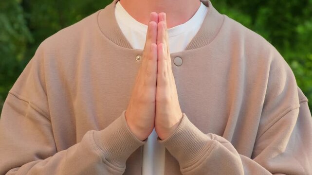 Hands in a prayer positong. Man doing a prayer. Close up of a person holding palms together in a prayer outdoors. Religious hand sign.