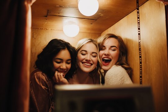 Warm candid moment of friends laughing inside a vintage photo booth, perfect for lifestyle, friendship, and nostalgia-themed visuals.