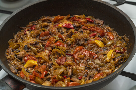 Photo of a roasted vegetable stew in brightly colorful colors on black frying pan. The ingredients consist of mushrooms, tomatoes, lemon, onions, fat, oil, seasonings, bell pepper. Home cooking