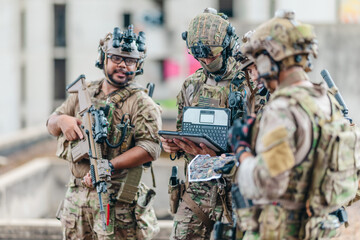 Fototapeta premium Military tactical team reviews mission plan on rugged laptop during outdoor field briefing
