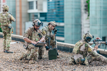 Fototapeta premium Military tactical team reviews mission plan on rugged laptop during outdoor field briefing