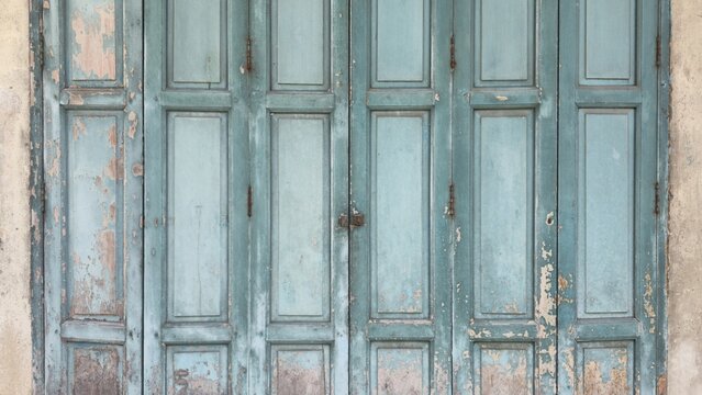 Antique green folding wooden door vintage texture background. Old retro style wooden folding door with distressed peeling teal paint and rustic texture details. 