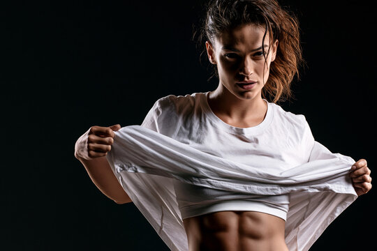 Athletic woman lifts her t-shirt in a studio to reveal toned abs. Fitness, workout, strength, health, athleticism, body positivity, training, wellness, lifestyle, sport and diet, consistency.