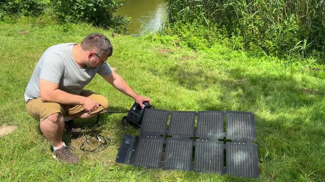 Man connecting a portable power station to foldable solar panels outdoors. Concept of renewable energy, off-grid electricity, sustainable technology, camping and clean portable power.