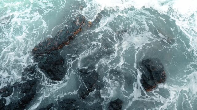 Ocean waves breaking over lava rocks near Isabela Island. Top down aerial view of pale turquoise water and white foam surrounding dark volcanic formations.