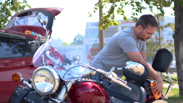 Slow motion video of a middle aged motorcyclist carefully wipes off dust from his motorcycle. He wipes the motorcycle seat with a rag after applying polish. Cropped 4K footage.