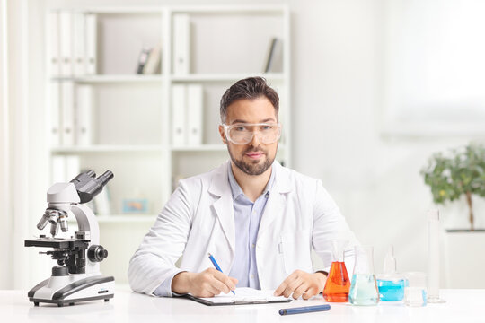 Scientist sitting at a desk with a microscope and chemical flasks