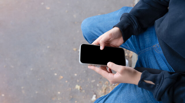 School boy holding smartphone with blank screen while waiting for school bus. Back to school concept Mobile phone mockup, student technology, education, communication and copy space.
