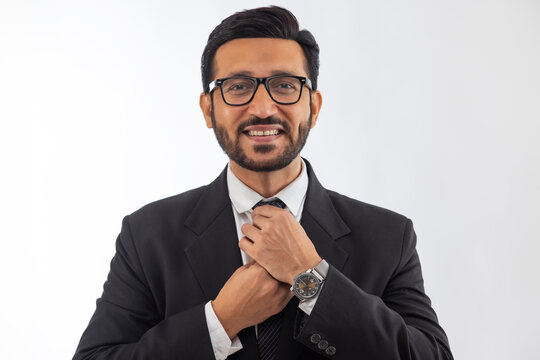Portrait of a corporate employee in formal business suit smiling and adjusting his necktie against plain backdrop.