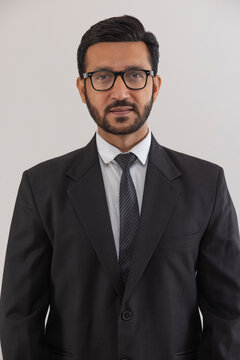 Portrait of a corporate employee in formal business suit standing against plain backdrop.