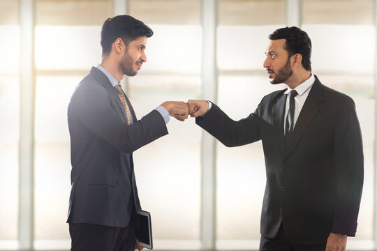 Corporate employees in formal business suit standing While making fist bump looking at each other.