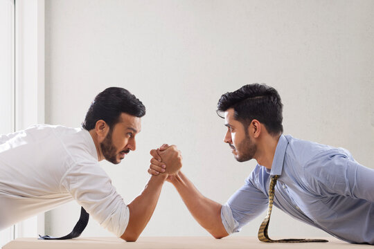 Corporate employees in formal clothing engaged in an arm wrestling match.