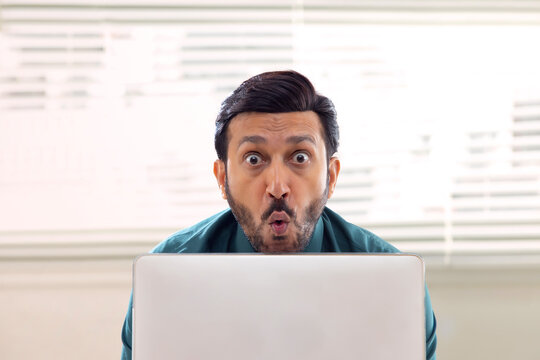 A corporate employee in formal clothing sitting behind laptop with goofy expression in office.